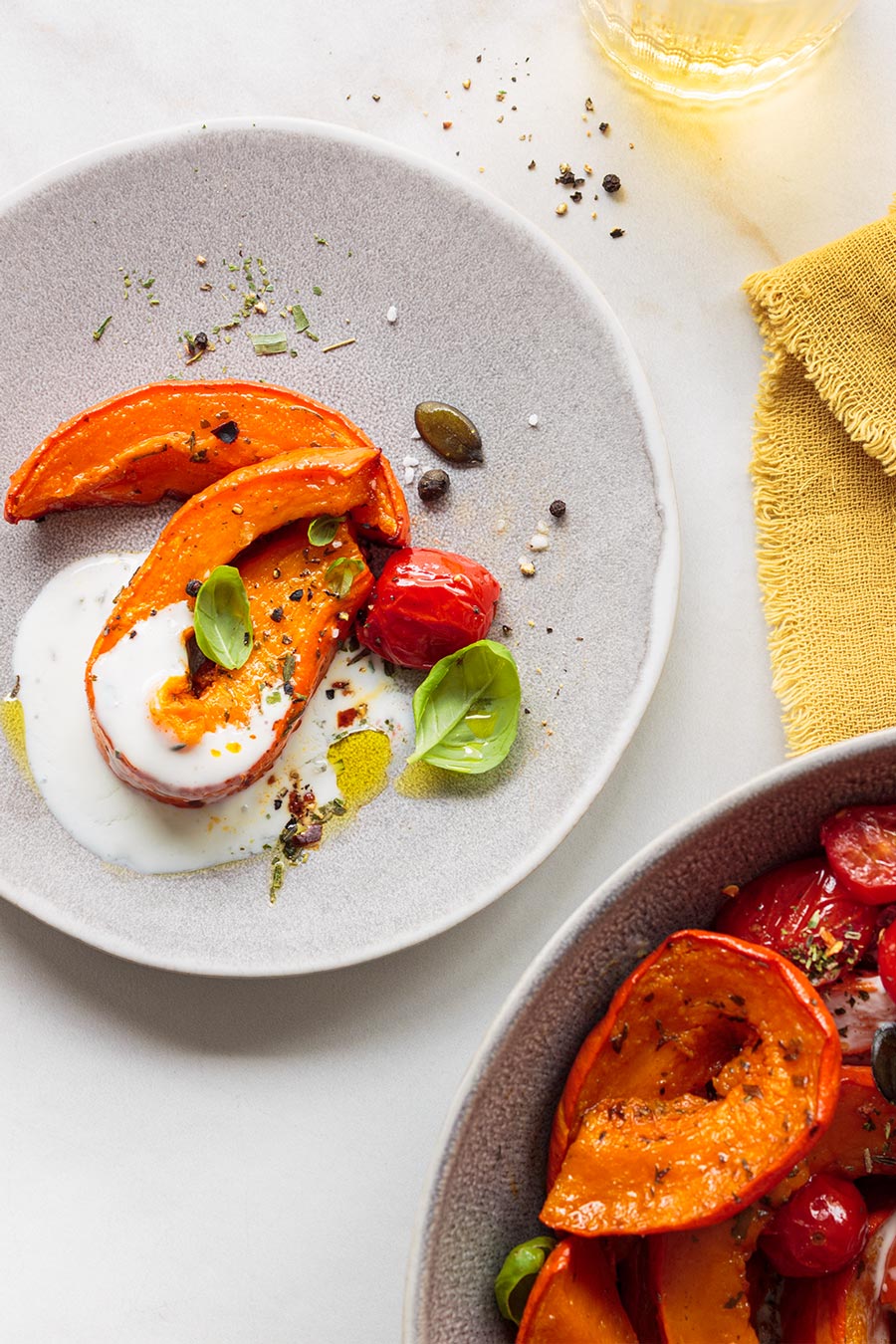 Gebackener Kürbis mit gerösteten Tomaten und Joghurt-Dressing – helle Food-Fotografie mit Basilikum und gelber Serviette