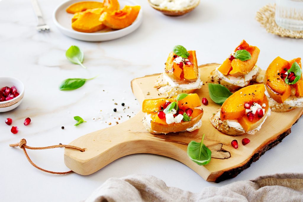 Baguette-Crostini mit gebackenem Kürbis auf Holzbrett – moderne, helle Sommer-Inszenierung in klarer Food-Fotografie im Querformat- fingerfood im Sommer - foodfotografie - natalia tag