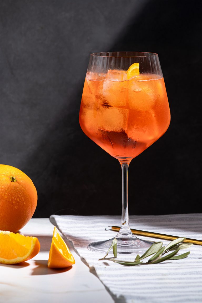 glas mit aperol und orange, klarer setaufbau, hell-dunkel kontrastiert durch knalliges orange, modernes und ästhetisches styling – foodfotografie von natalia tag