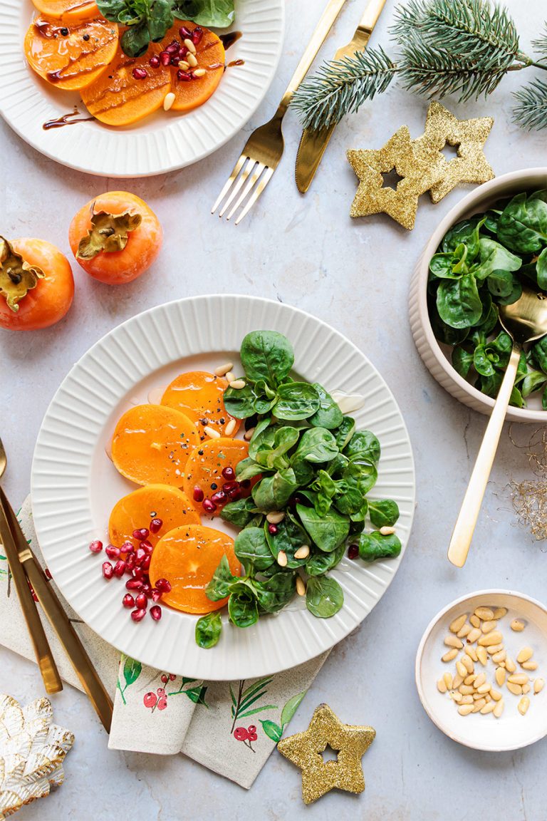 teller mit kaki-carpaccio und feldsalat, weiches winterlicht, weihnachtliche deko, gemütliche stimmung, frische und genuss – foodfotografie von natalia tag