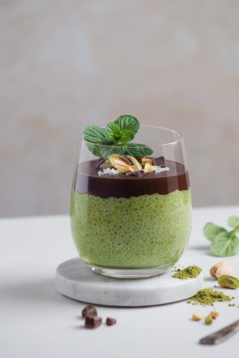 mint-chia-matcha-dessert in hellem set, oberfläche mit dunkler schokolade, pistazien und schokostückchen dekoriert, modernes und klares styling – foodfotografie von natalia tag