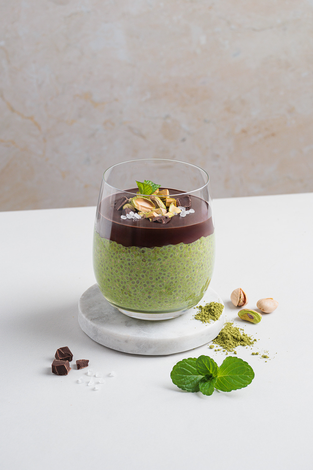 mint-chia-matcha-dessert in hellem set, oberfläche mit dunkler schokolade, pistazien und schokostückchen dekoriert, modernes und klares styling – foodfotografie und Produktfotografie von natalia tag