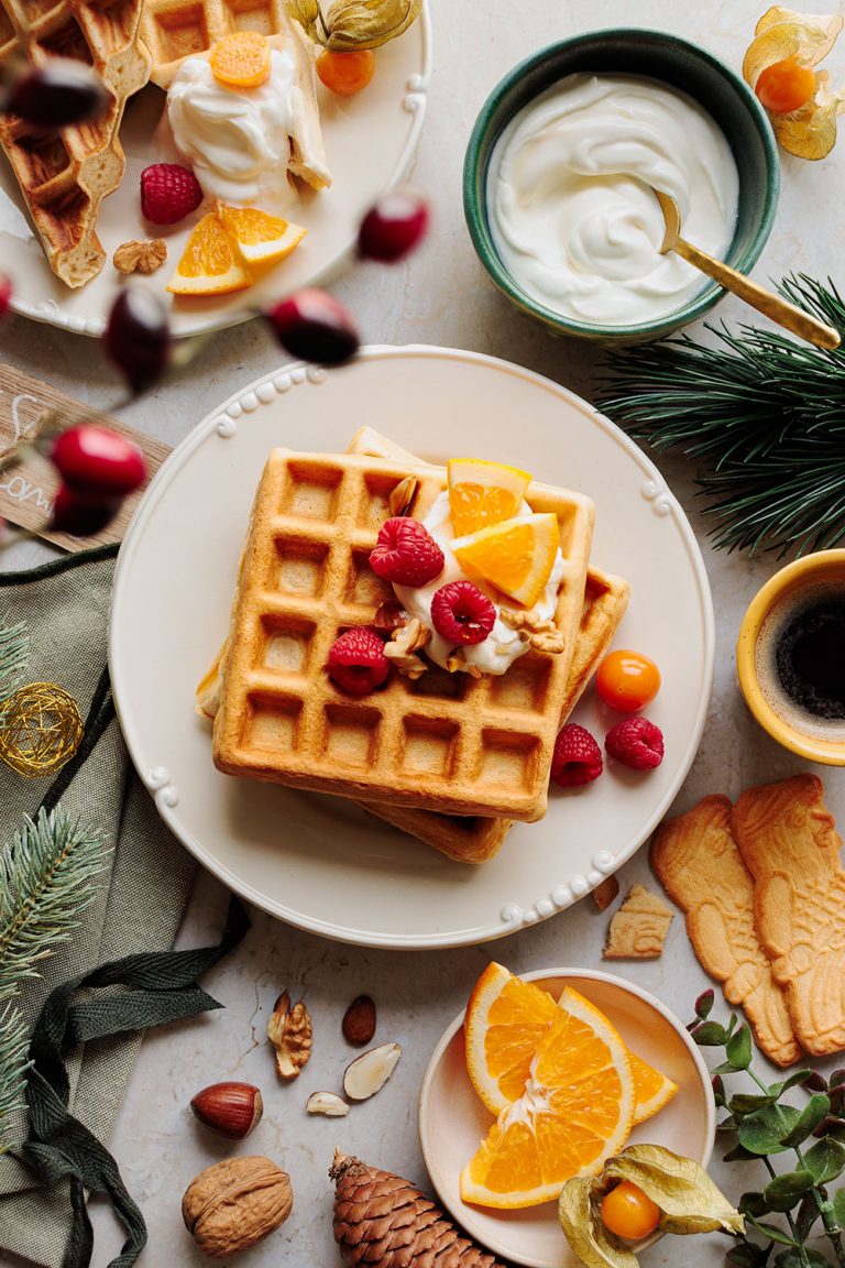spekulatius-orangen-waffeln mit protein auf teller, weihnachtliches brunch-setup mit tasse kaffe und tannenzweigen, weiches licht, gemütliche festliche stimmung – foodfotografie von natalia tag