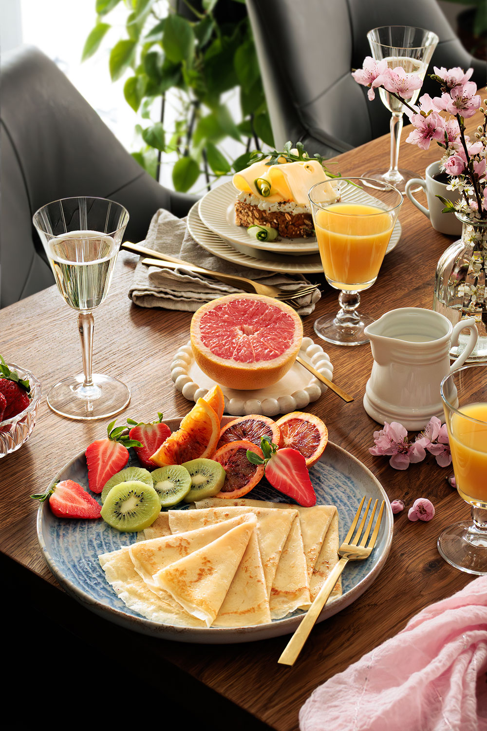 Gedeckter Frühstückstisch, gemütliche einladende Atmosphäre, frisches Obst, Pfannkuchen, Käsebrot, zwei Gläser Sekt, in der Mitte eine frische aufgeschnittene Grapefruit – moderne Foodfotografie Natalia Tag